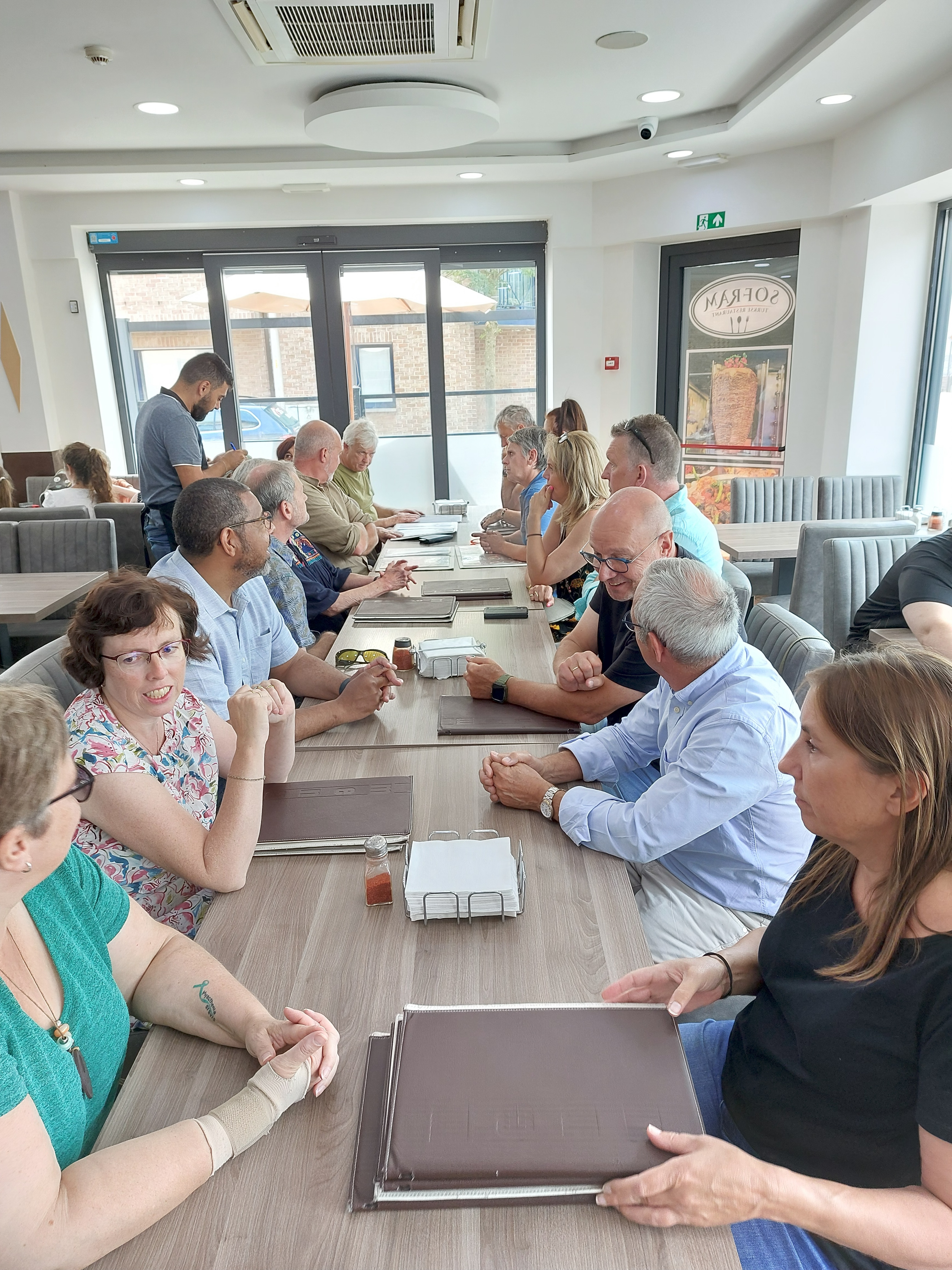 groep van mensen met een visuele en/of auditieve beperking met hun begeleiders die rond een lange tafel zitten.