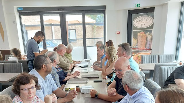 groep van mensen met een visuele en/of auditieve beperking met hun begeleiders die rond een lange tafel zitten.