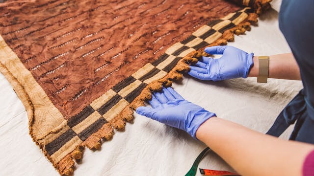 Medewerker van het Collectiebeheerteam onderzoekt een geweven doek.