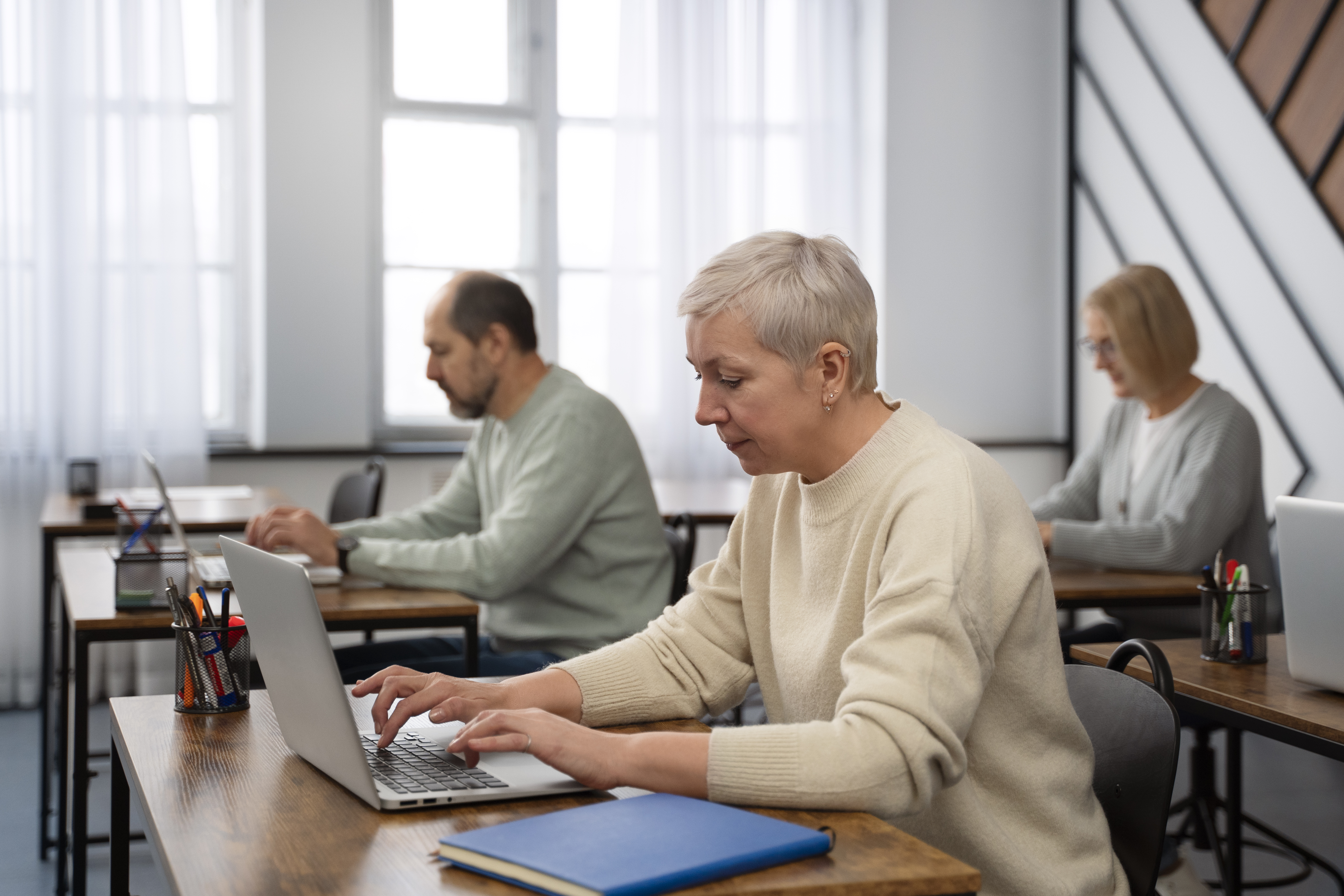 3 personen die in een zaal zitten en bezig zijn op hun laptop