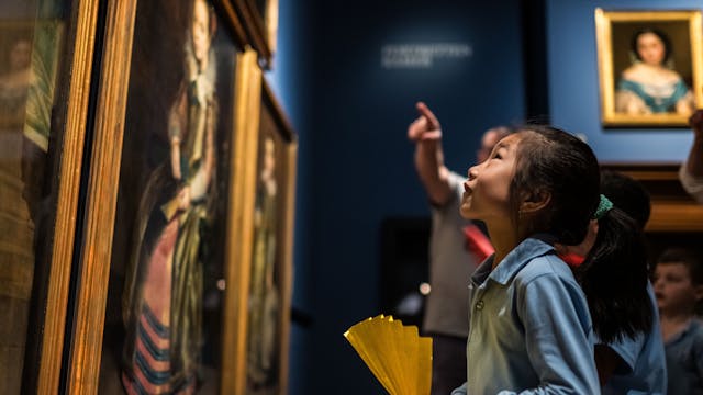 Een kindje kijkt naar enkele schilderijen in een museumzaal.