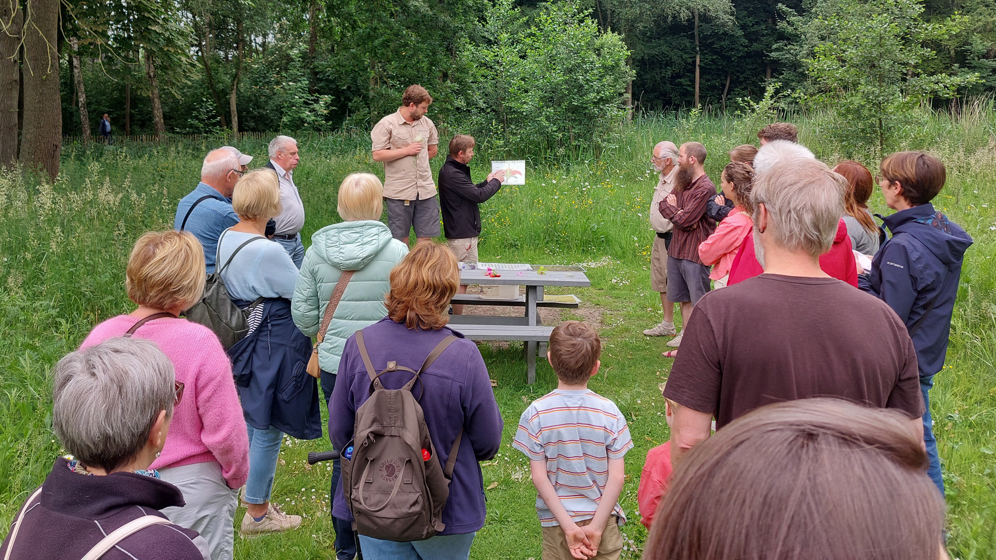 In een natuurlijke omgeving luistert een groep mensen naar een uitleg van een gids.