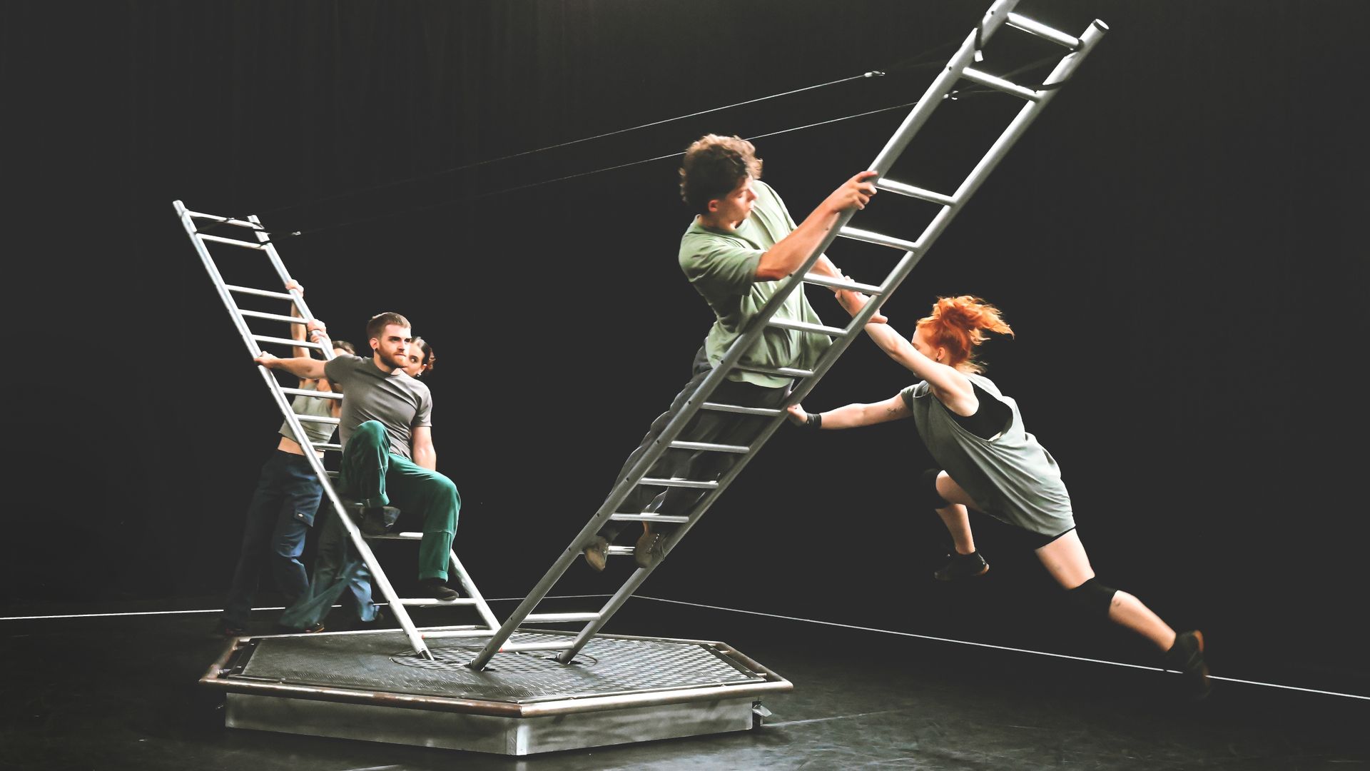 Artiesten hangen aan en balanceren op schuine ladders.