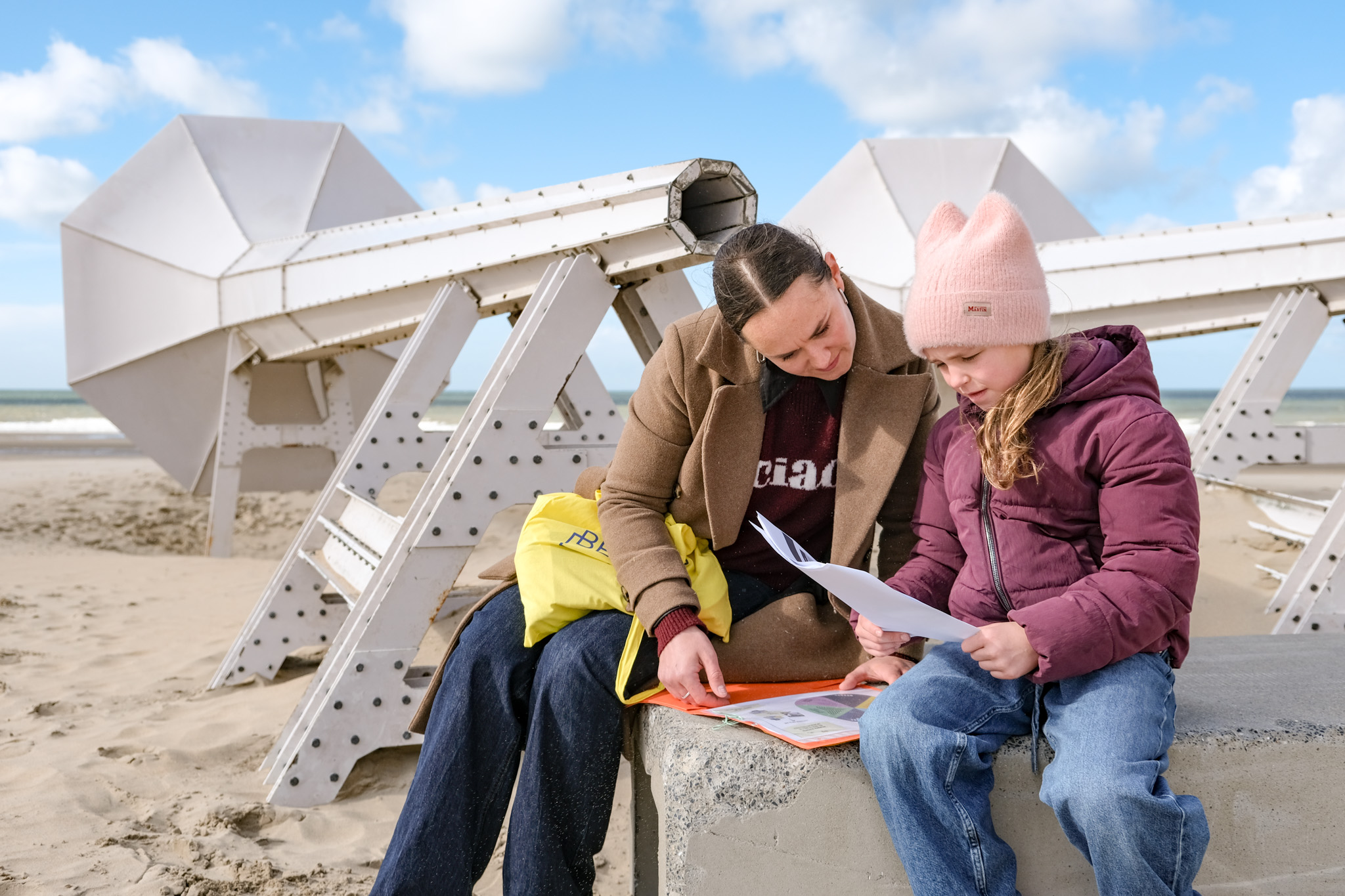 Moeder en kind kijken naar de opdrachtenkaart, met een kunstwerk van Beaufort op de achtergrond.