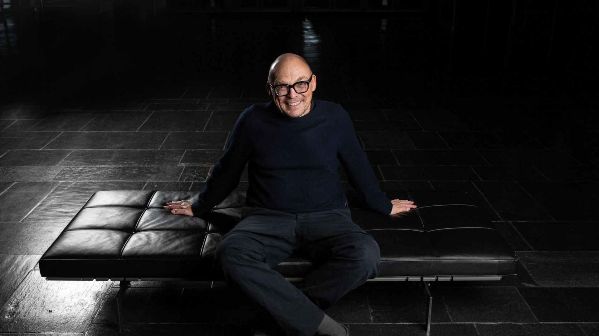 Muzikant Bugge Wesseltoft in zwarte kledij op zwarte zetel in zwarte ruimte.