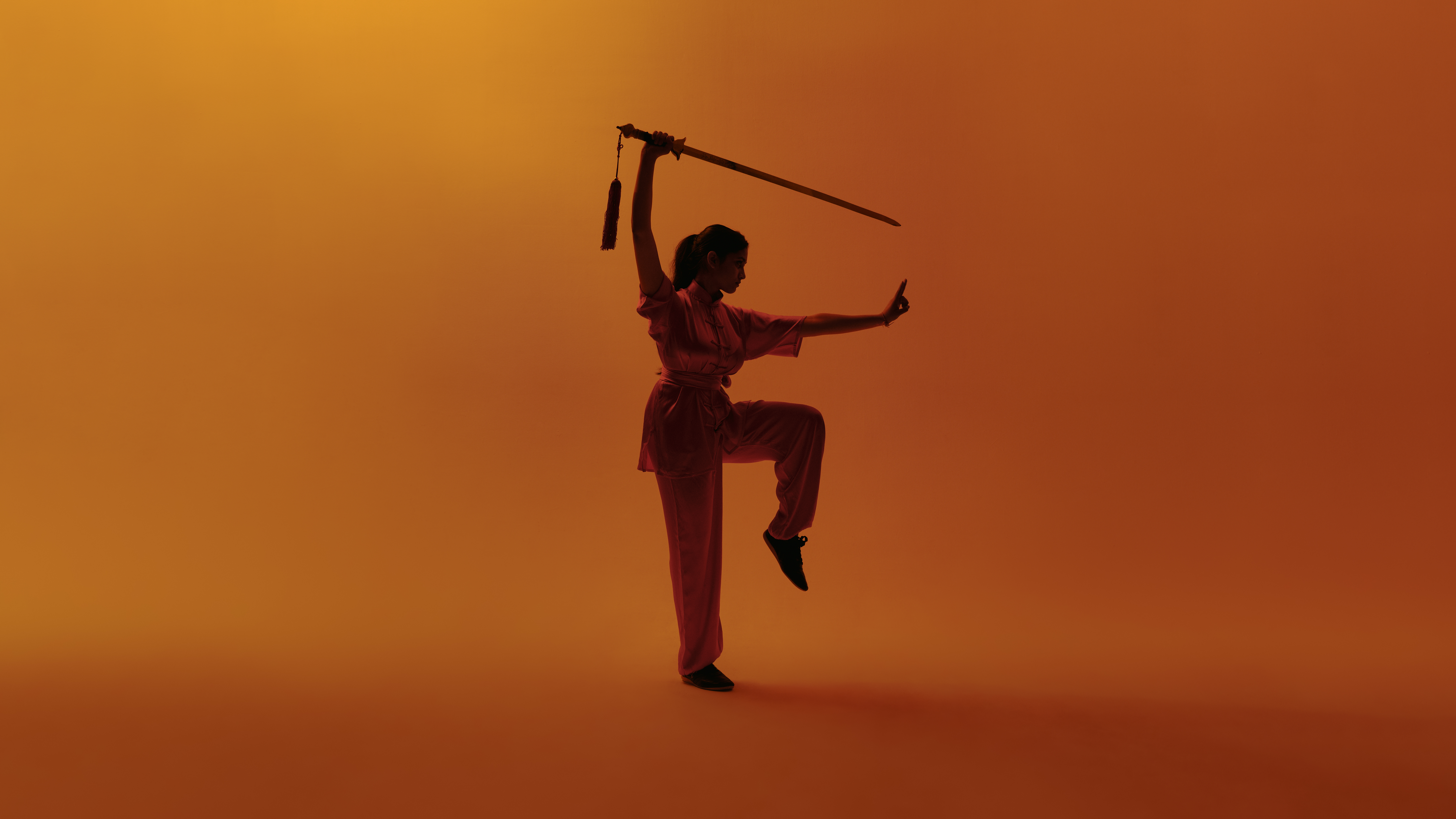 Wushu pose met zwaard op oranje achtergrond