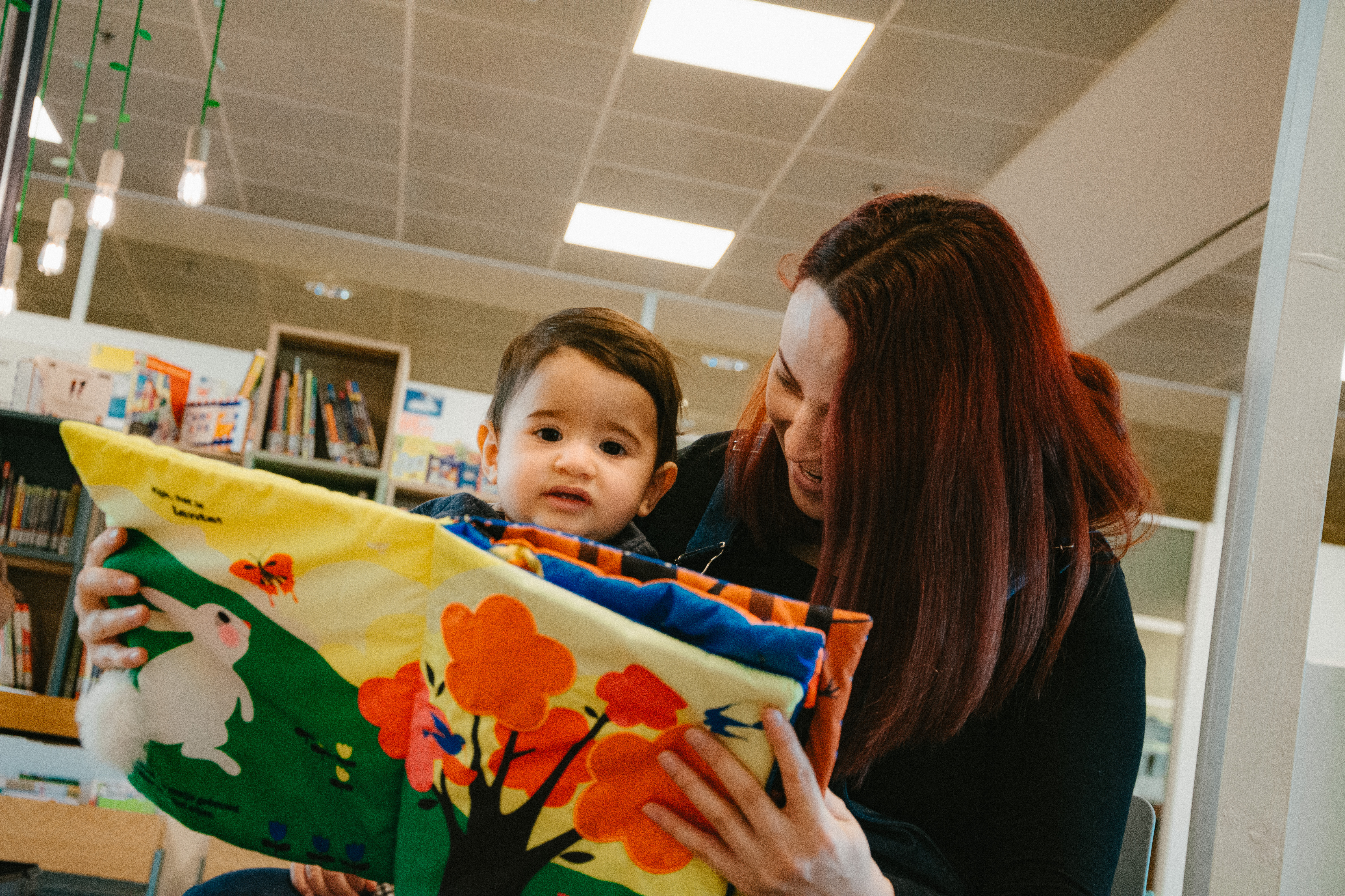 Mama met peuter op schoot leest stoffenboekje voor 