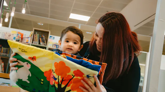 Mama met peuter op schoot leest stoffenboekje voor