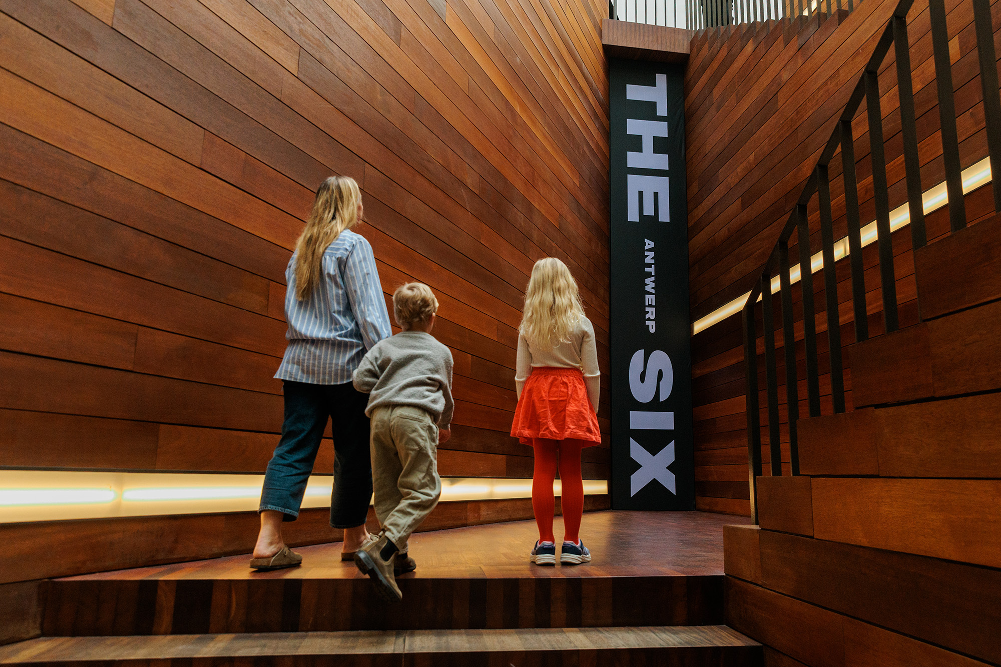 Moeder met 2 kinderen kijkt naar de banner van De Antwerpse Zes