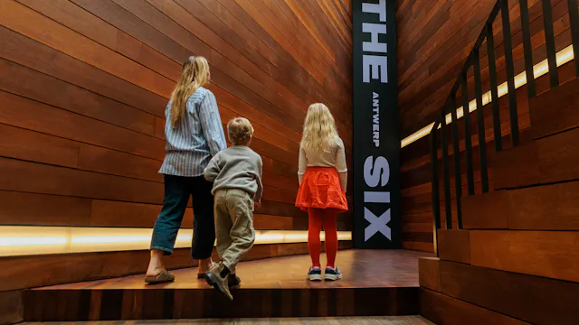 Moeder met 2 kinderen kijkt naar de banner van De Antwerpse Zes