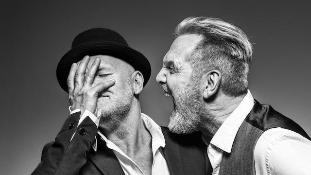 Zwart-witbeeld van Raf die schreeuwt tegen broer Mich; Mich trekt hoofd weg en schermt gezicht af met hand.