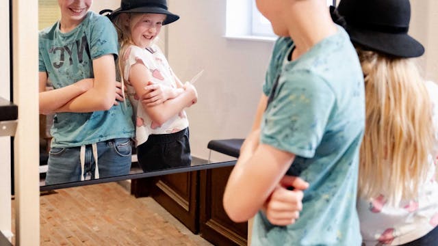 Twee kinderen met een oude hoed poseren lachend voor de spiegel