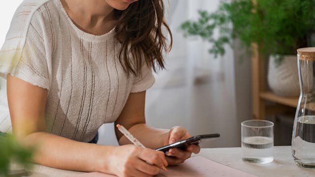 dame die iets opzoekt op de smartphone en ondertussen nota neemt in een schrift