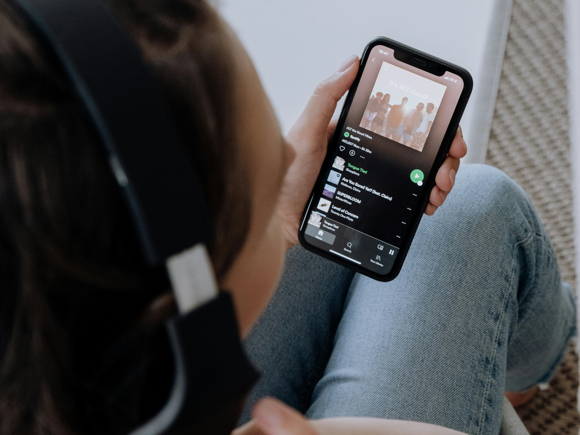 Persoon met hoofdtelefoon die smartphone vasthoudt waarop de Spotify-app geopend is