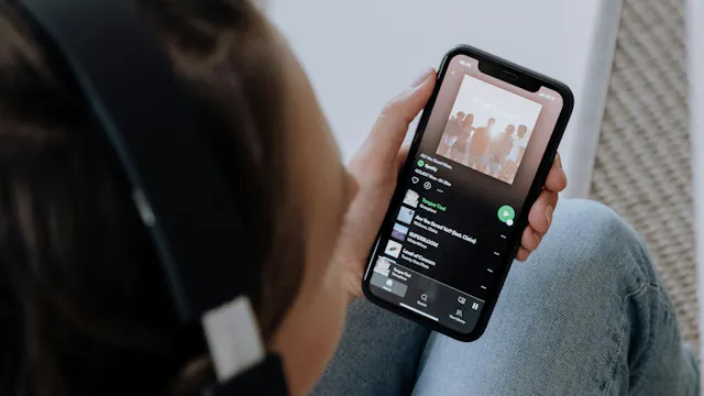 Persoon met hoofdtelefoon die smartphone vasthoudt waarop de Spotify-app geopend is