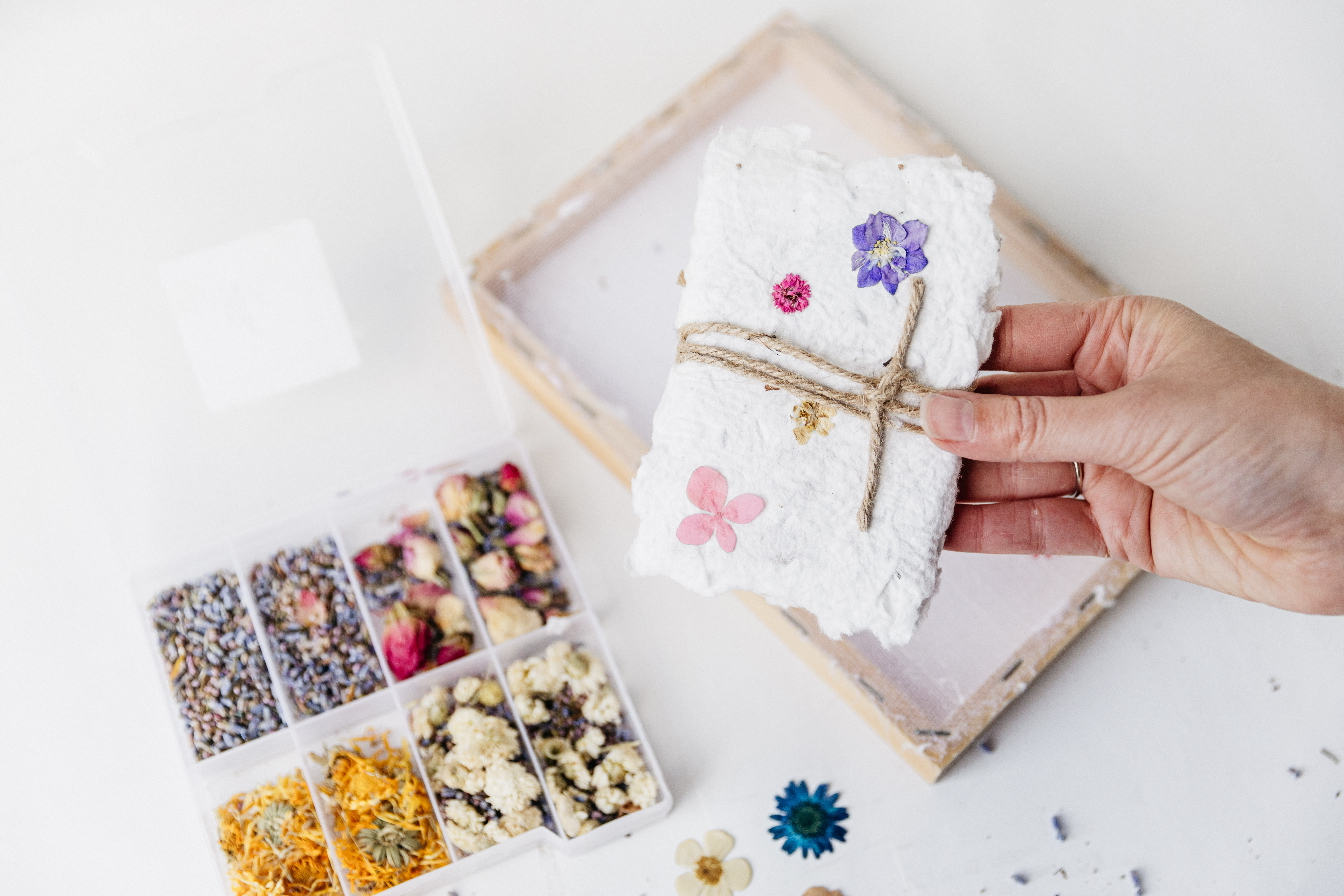 hand die handgeschept papier vastheeft, een schepraam en een doosje vol decoratie