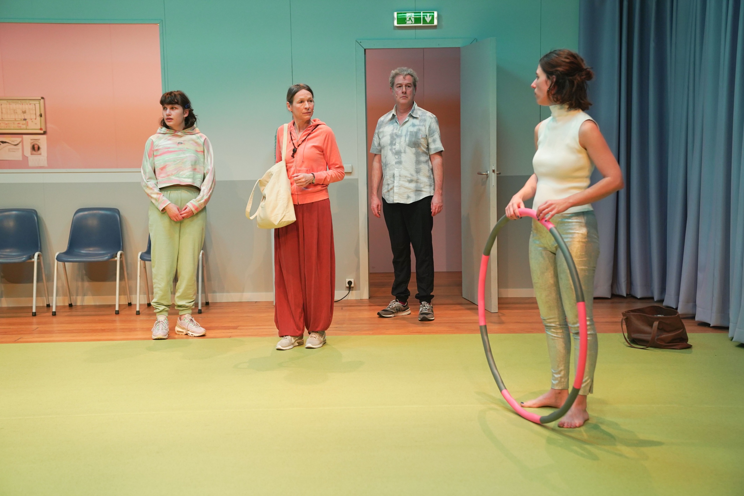 Vijf mensen in een theatersetting, met kleurrijke kleding en een hoelahoep.