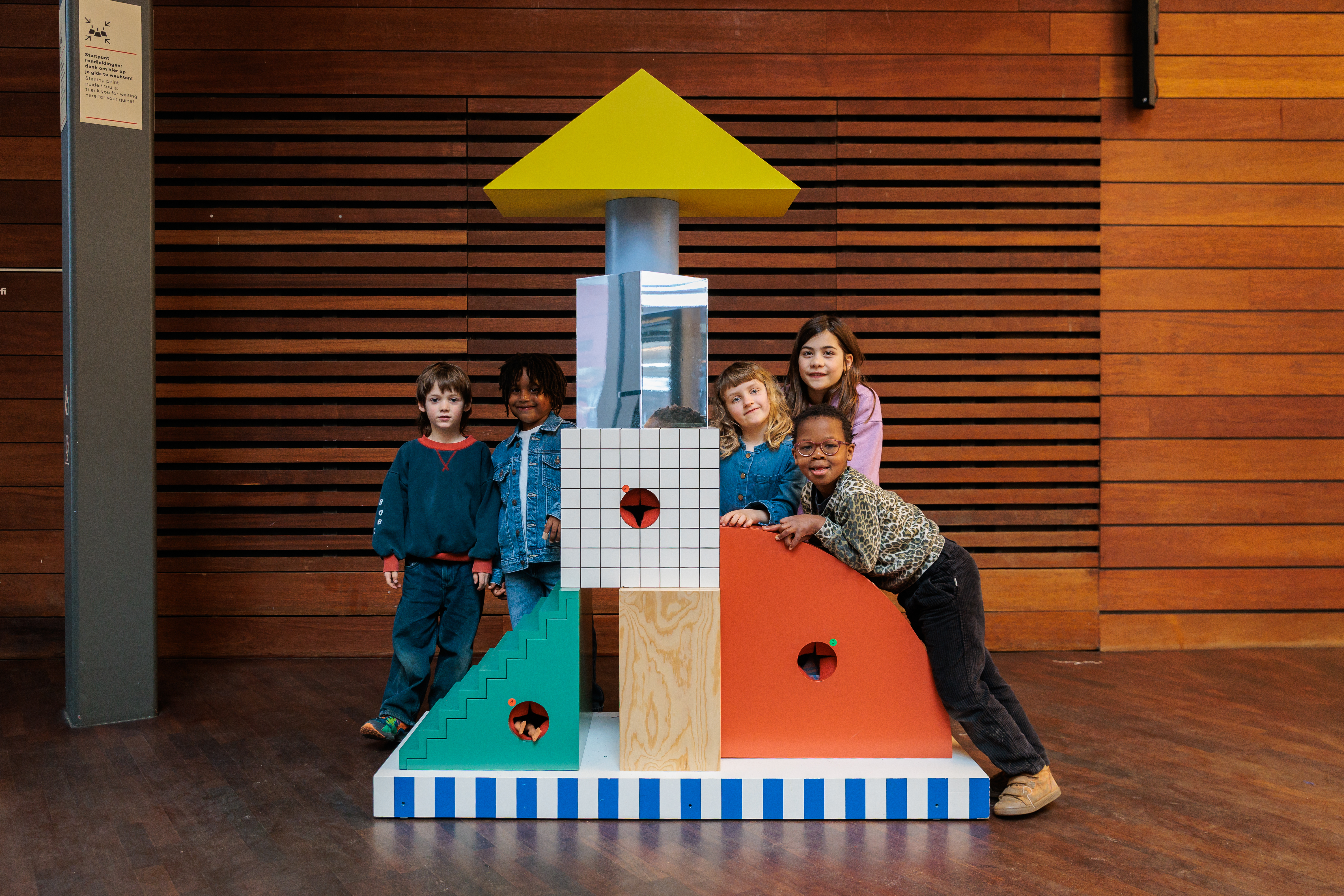 Kinderen leunen op een totem met speelse vormen en kleuren in de MoMu inkomhal