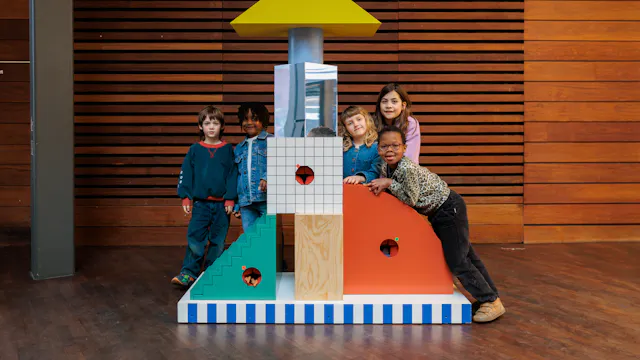 Kinderen leunen op een totem met speelse vormen en kleuren in de MoMu inkomhal