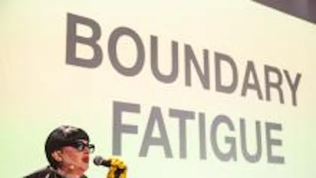 Afbeelding van persoon met microfoon vast voor een groot doek met tekst op geprojecteerd.