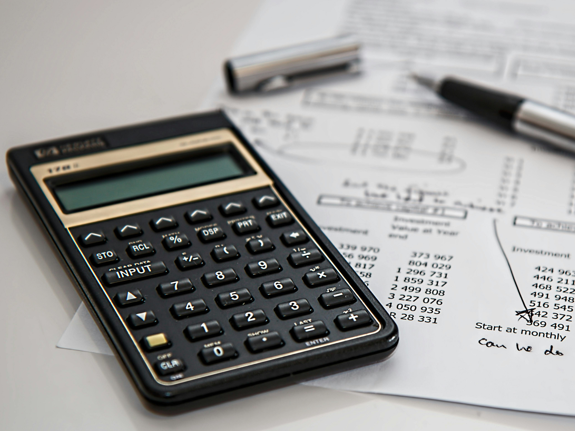 Rekenmachine, balpen en blad met uitgaven die op tafel liggen