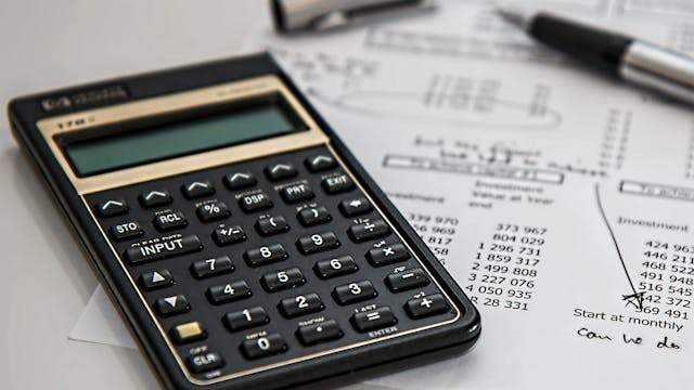 Rekenmachine, balpen en blad met uitgaven die op tafel liggen