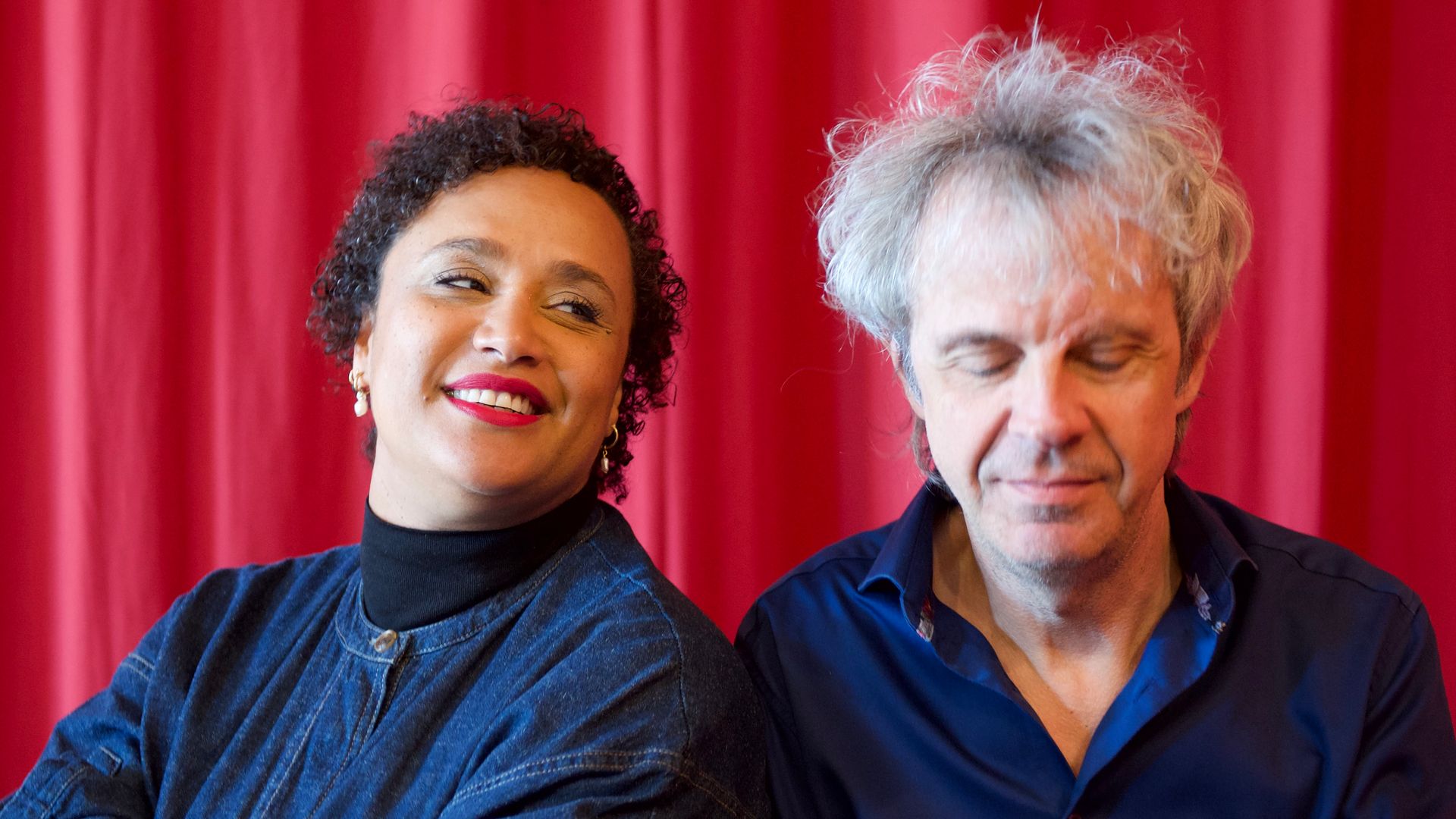 Twee muzikanten van Room 13 Orchestra voor een rood gordijn.