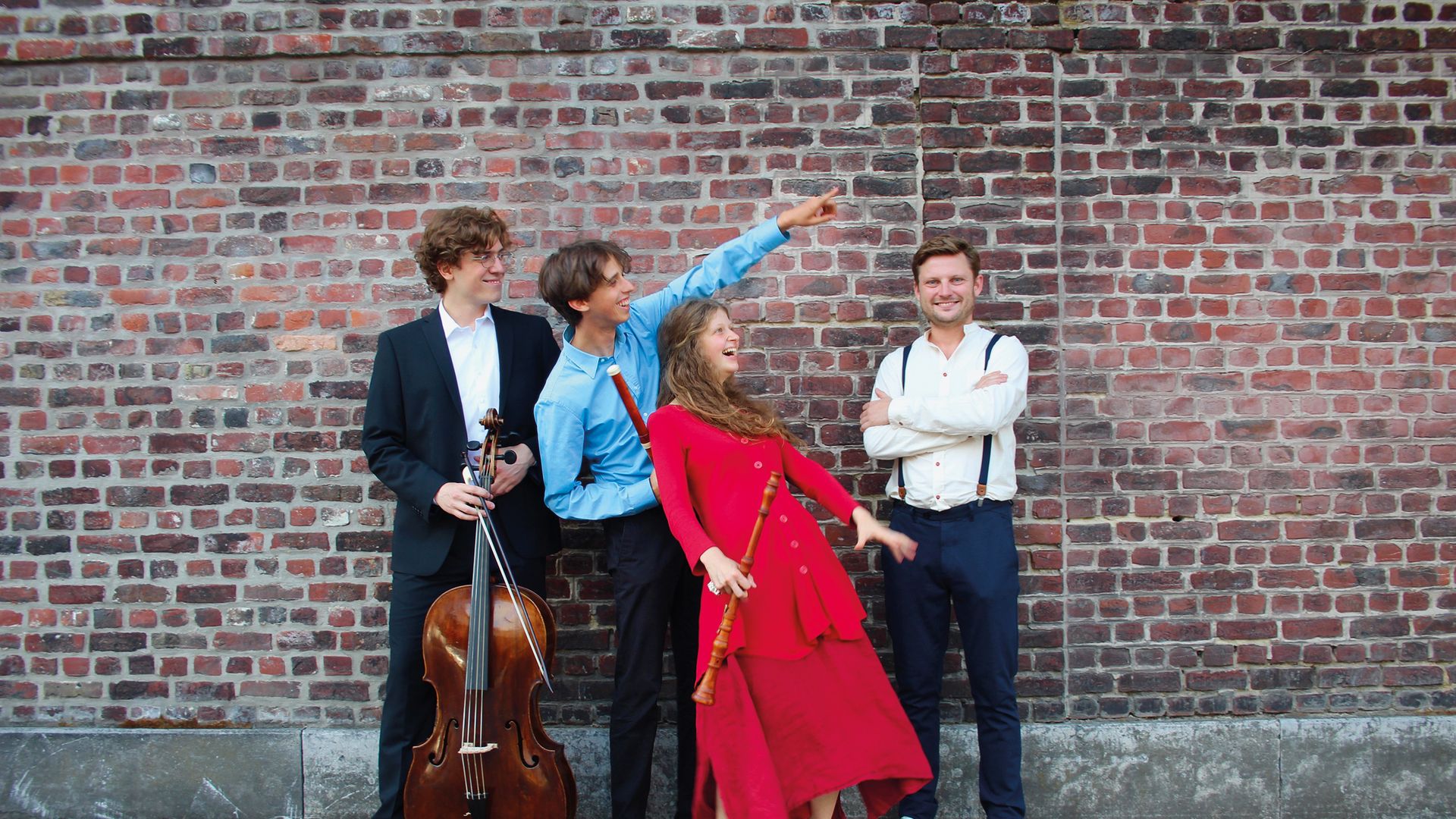Muzikanten Musica Gloria lachend en wijzend voor baksteenmuur