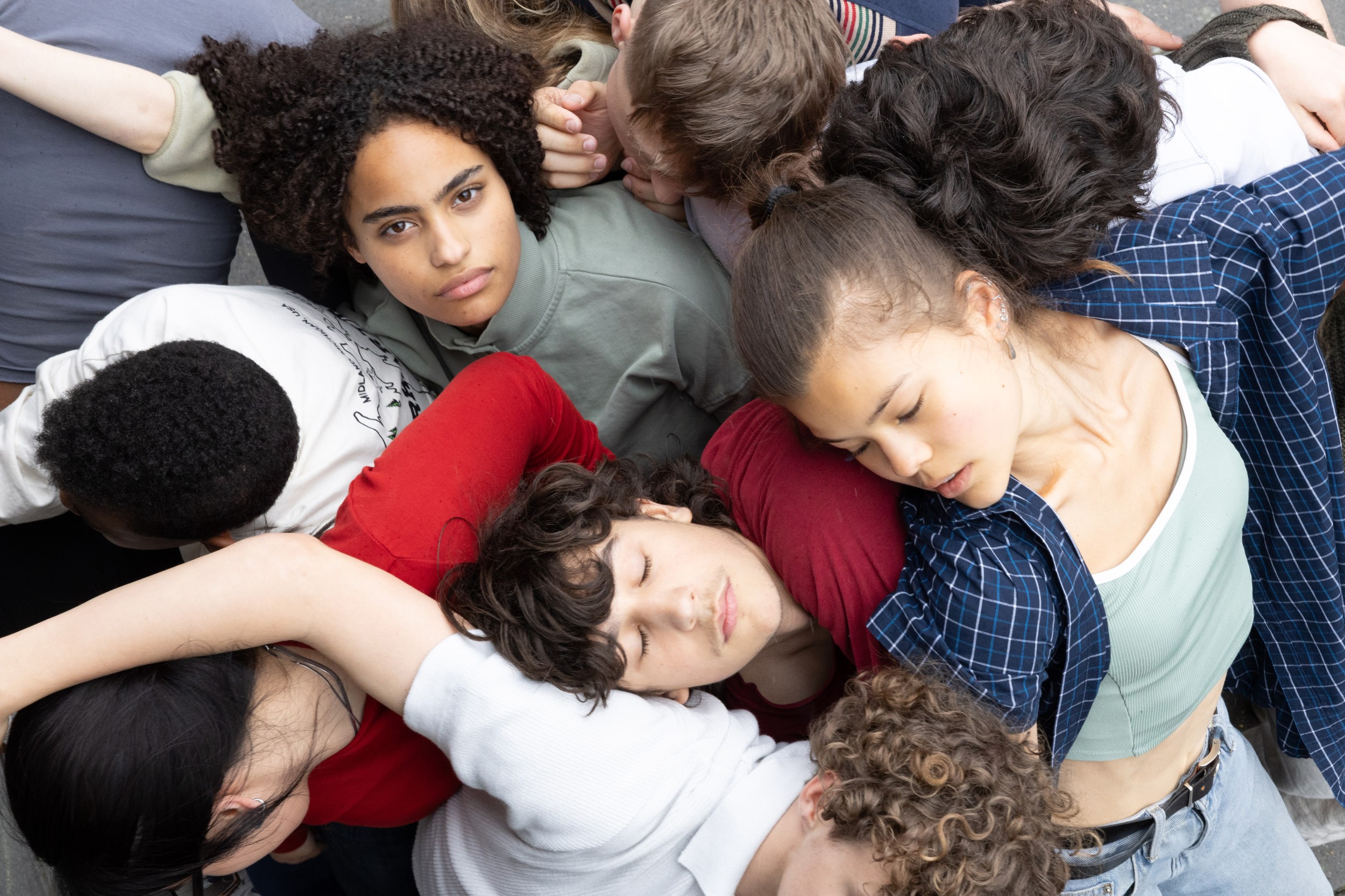 Groep jongeren ligt dicht op elkaar, met enkele slaperige gezichten en verschillende haardrachten.