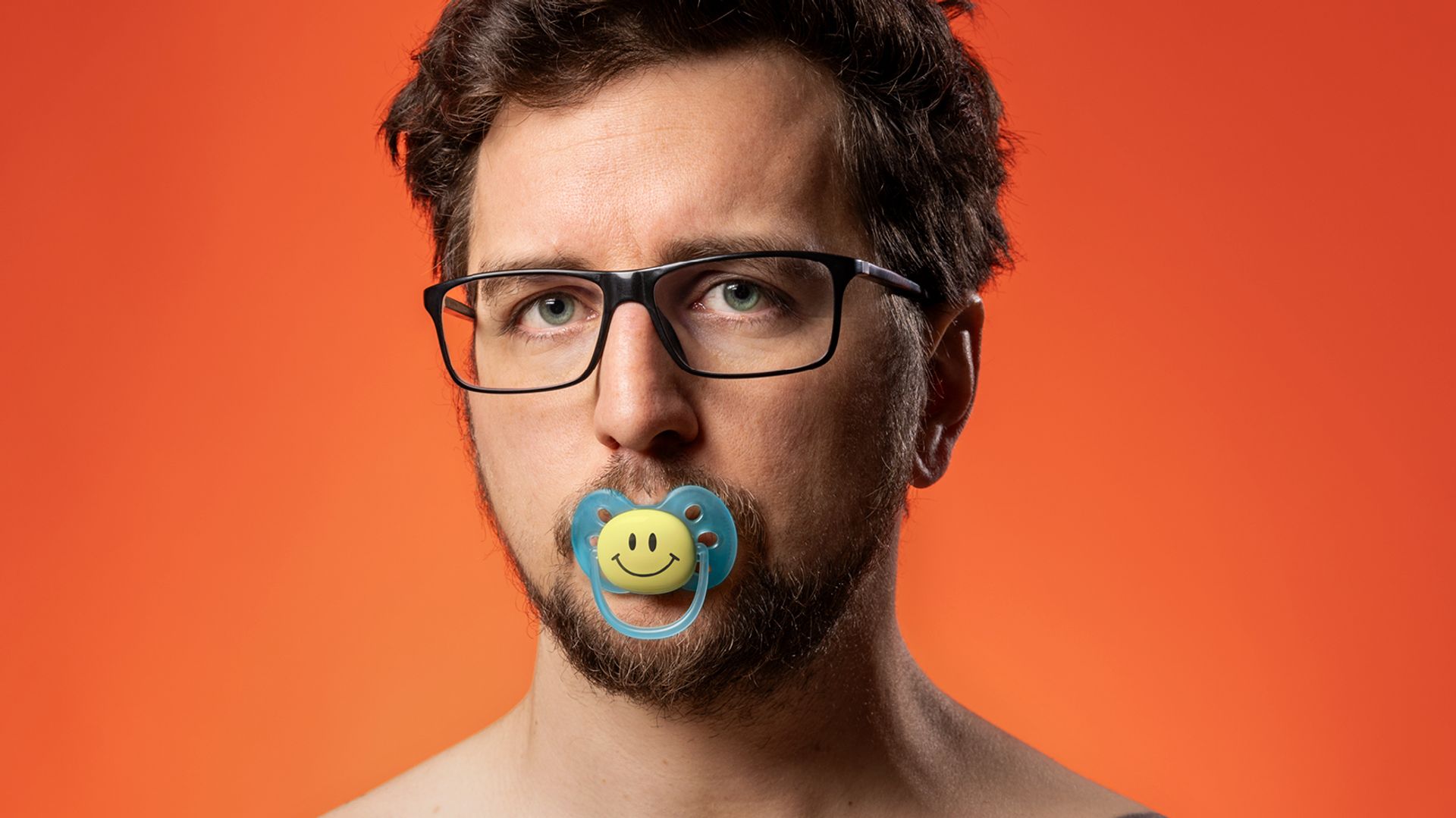 Jasper Posson met bloot bovenlijf en fopspeen met smiley in mond.