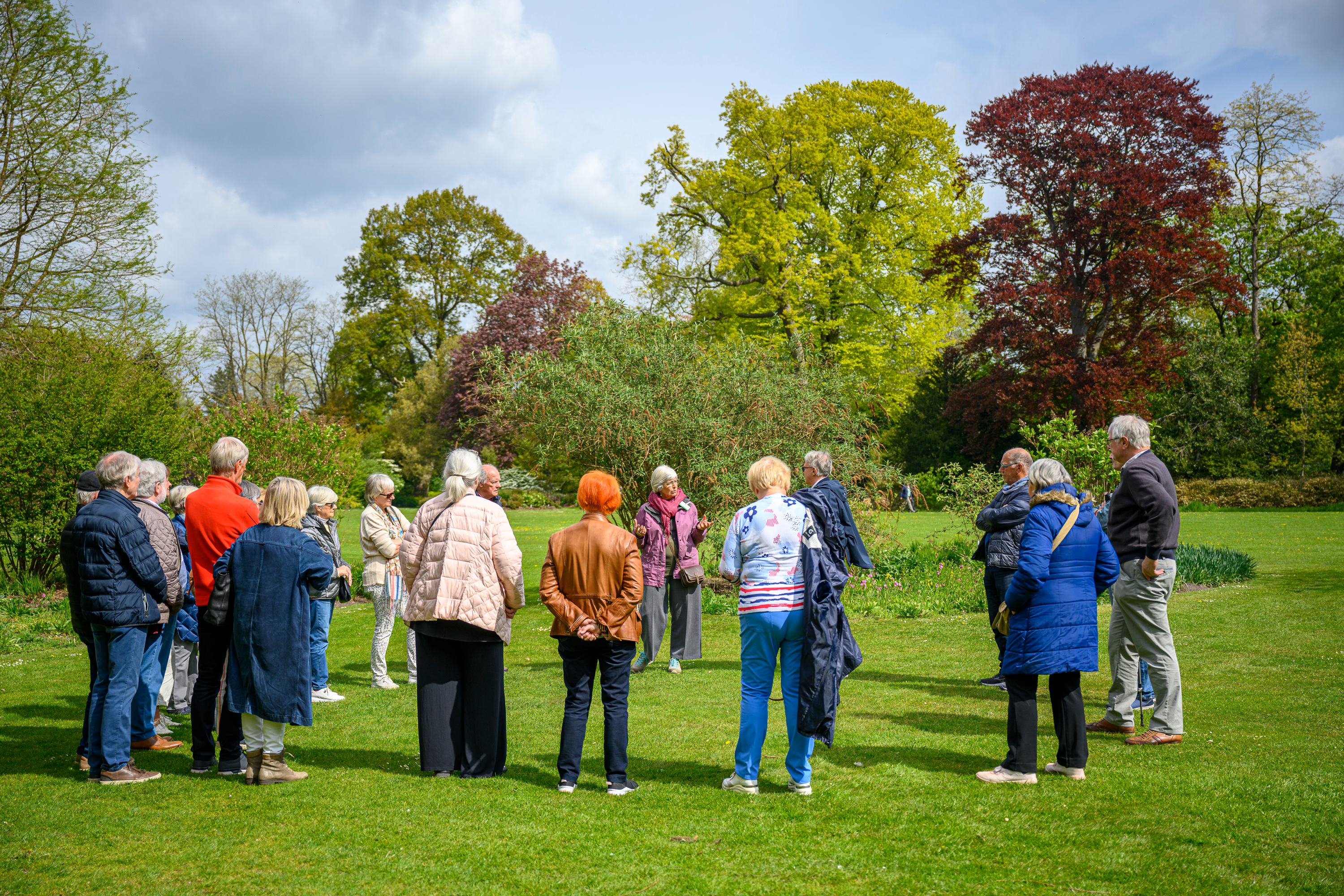 Gids vertelt in het arboretum aan een groep bezoekers die vrolijk gekleurde kleding dragen