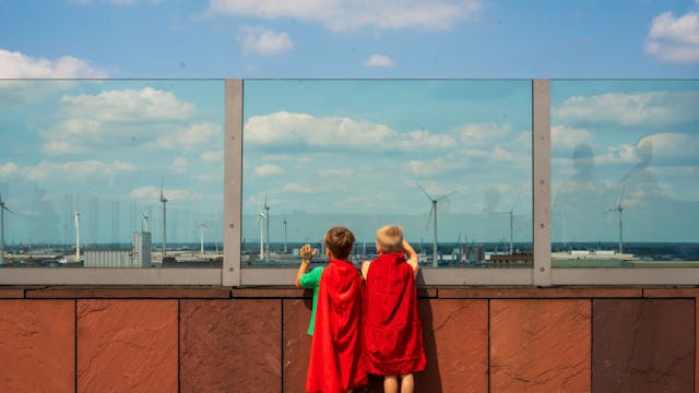 Twee kindjes met een cape kijken naar de skyline van antwerpen op het dak van het mas