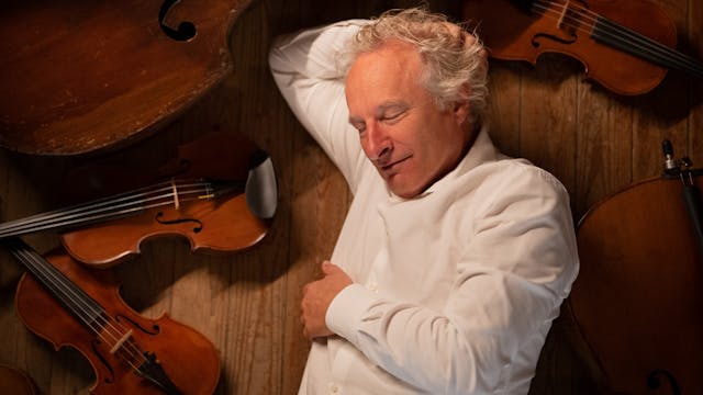 Man ligt ontspannen tussen verschillende violen en een grote cello.