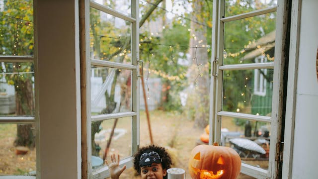 Kind kijkt door raam waar Halloween-pompoen op de vensterbank staat.