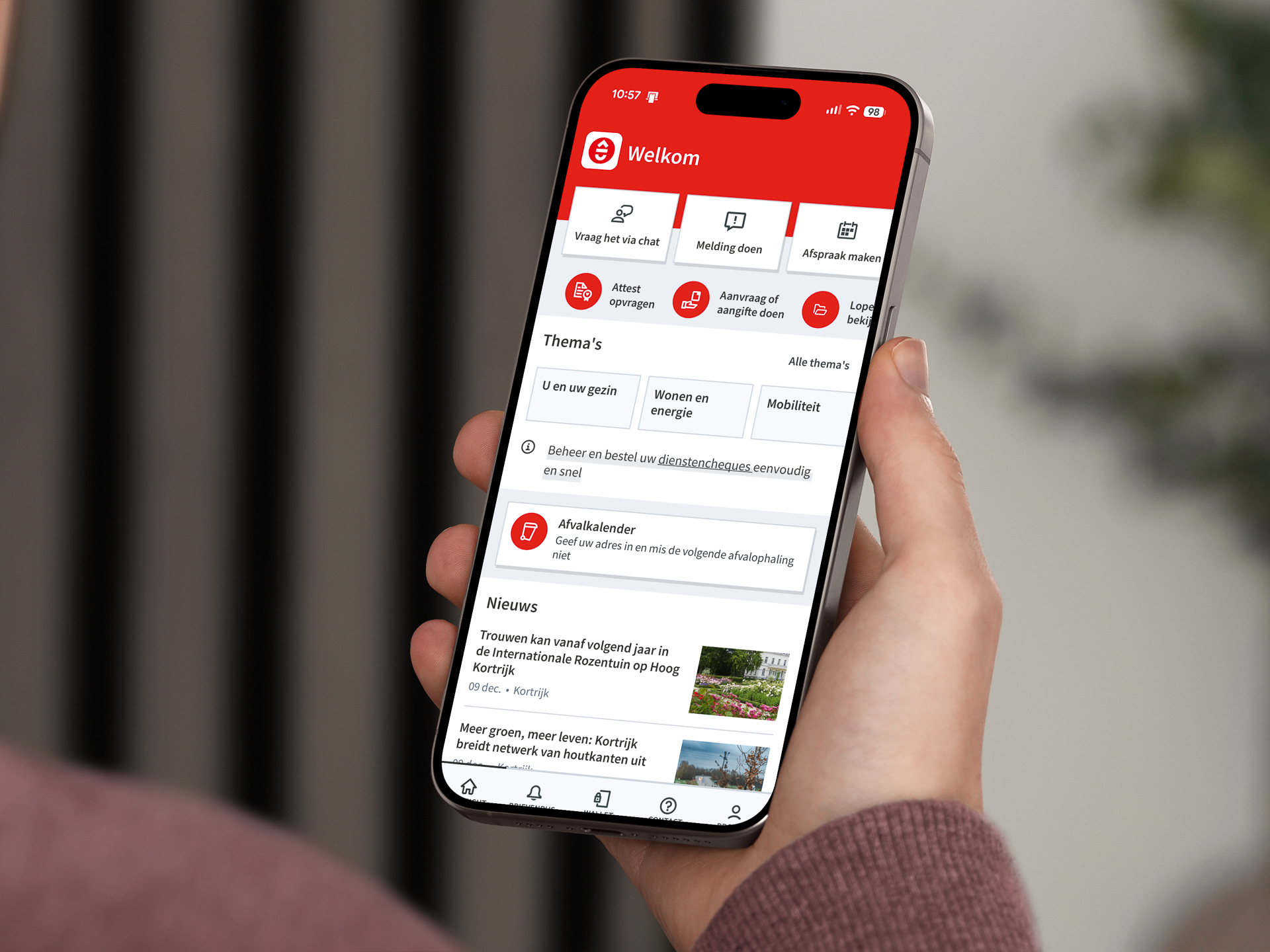 Hand die smartphone vasthoudt waarop het toegangsscherm van de Kortrijk-app te zien is: thema's, afvalkalender en nieuws