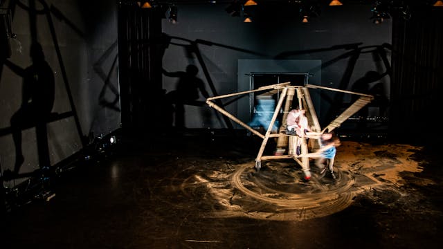Foto uit de voorstelling Oef!. Op het podium staat een houten installatie, de schaduwen ervan zijn rondom rond op de muren te zien.