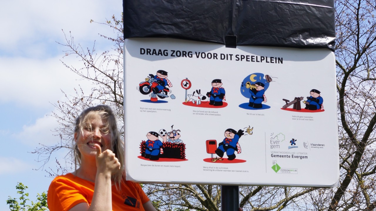 Een medewerker van Gemeente Evergem naast een bord van een speelplein