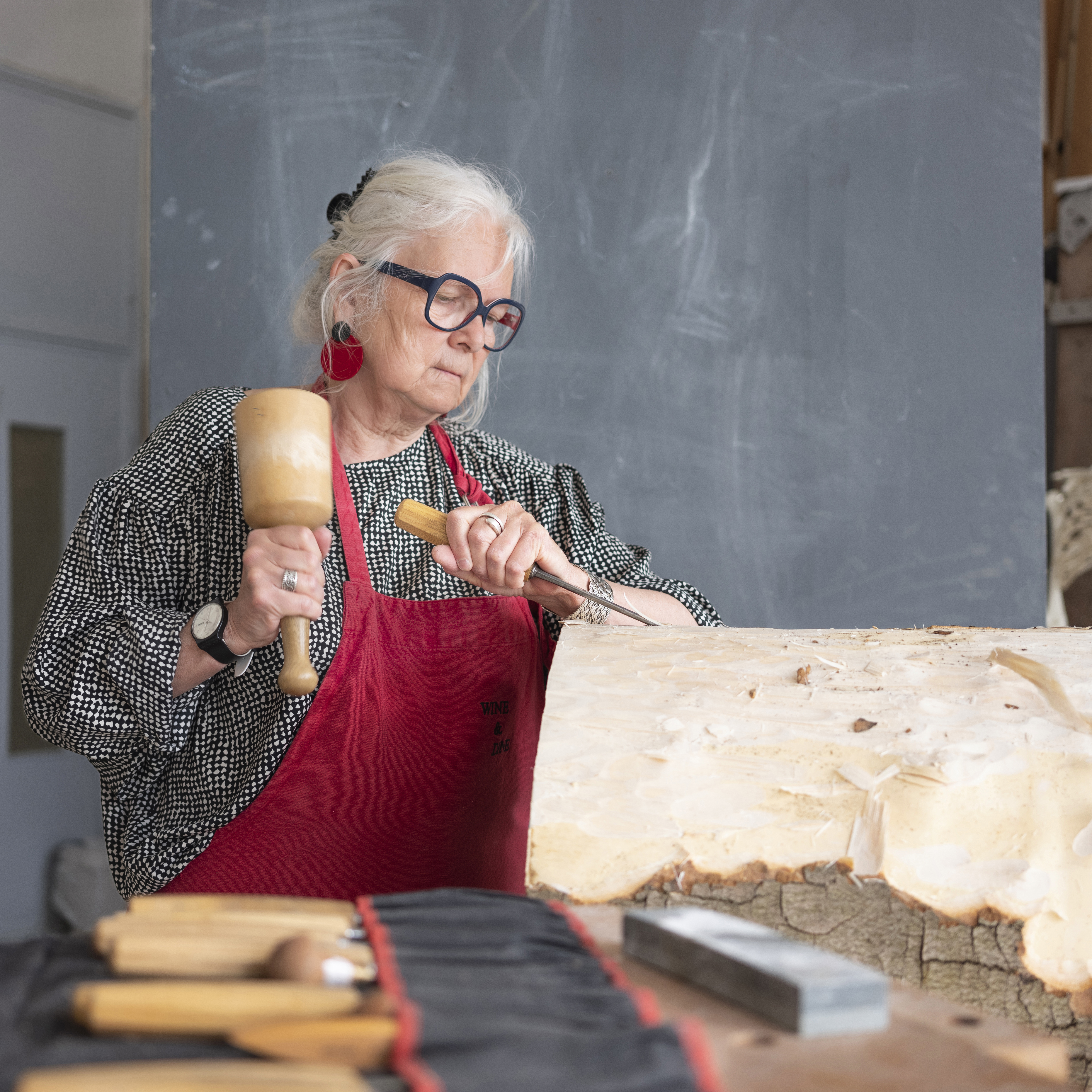 Dien De Bruyn bewerkt hout met beitel en hamer in een werkplaats.