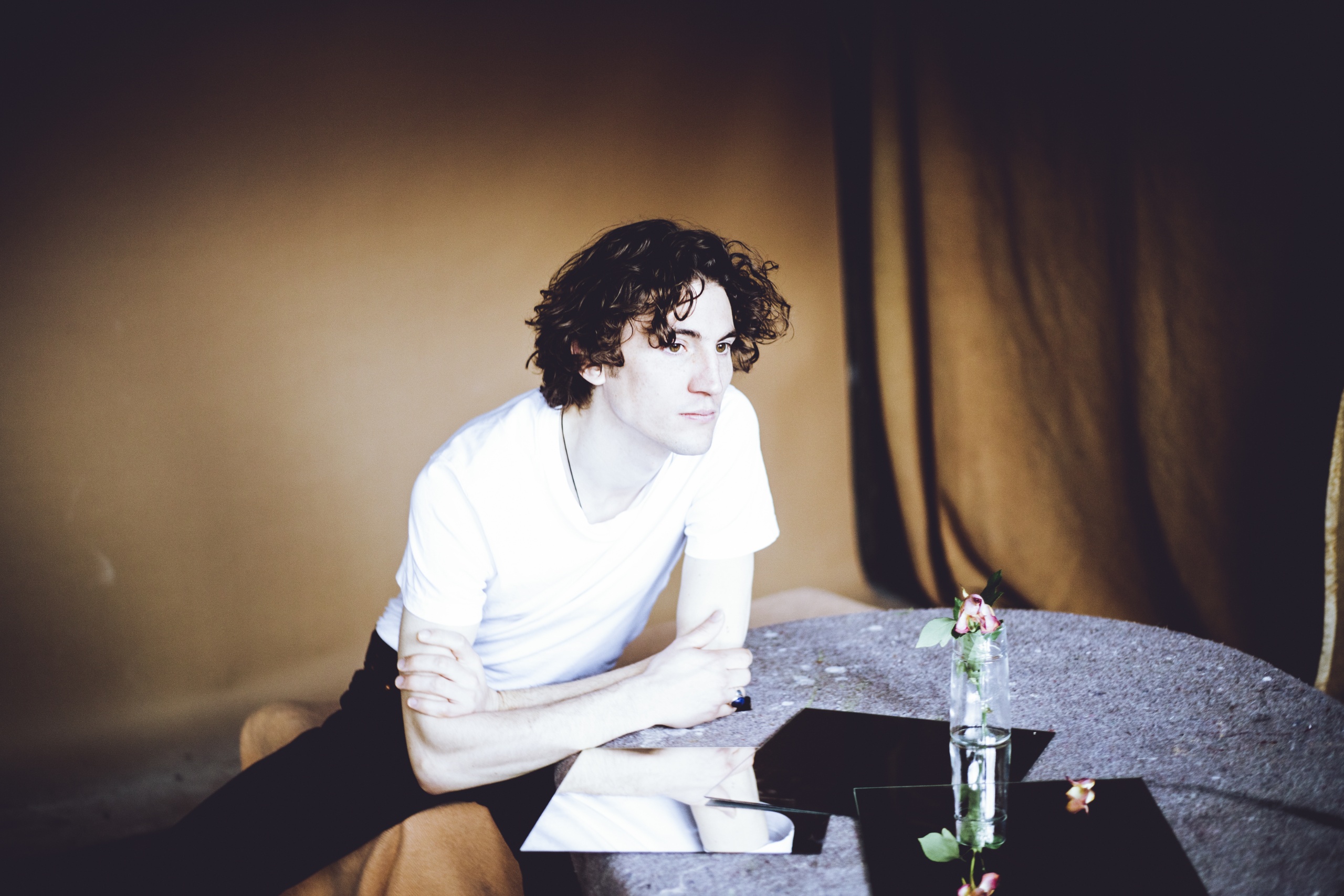 Jongeman in wit T-shirt leunend op een tafel met spiegels en bloemen.