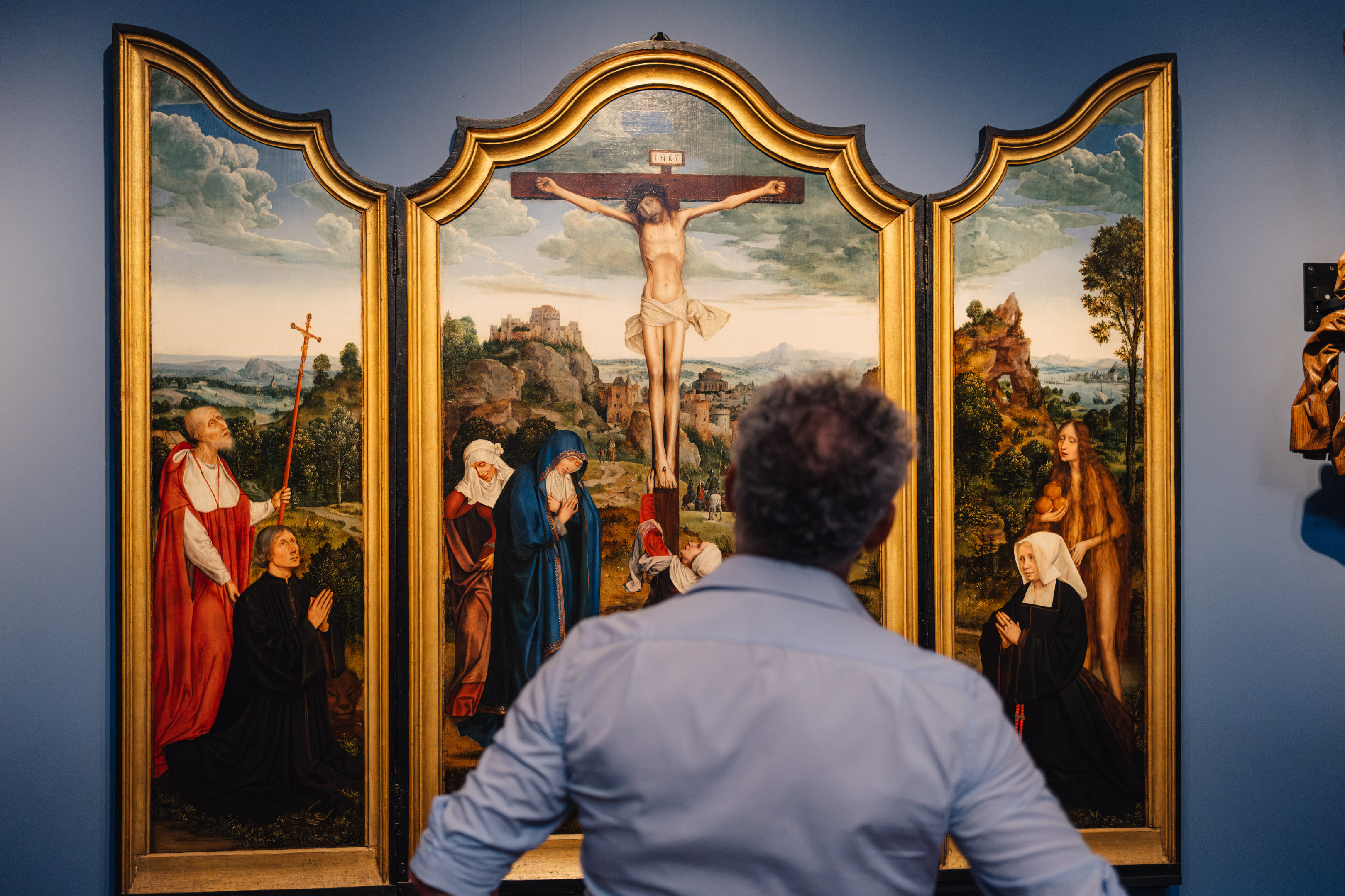 Een man kijkt naar het drieluik 'Calvarie met stichterspaar' van Quinten Massijs.