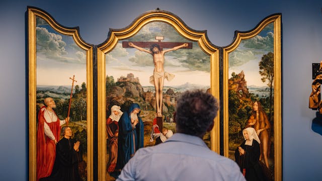 Een man kijkt naar het drieluik 'Calvarie met stichterspaar' van Quinten Massijs.