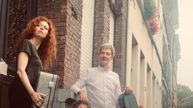 Drie mensen met muziekinstrumenten staan op een stoep voor een gebouw met bakstenen en bloemenbakken. Eén persoon staat met een gitaar, een ander zit op de treden met een viool en een derde persoon staat met een koffer en een gitaar.