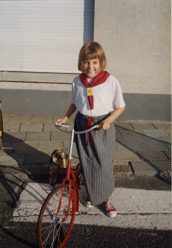Portret van de 9-jarige Femke (dochter van Rosita Fontenoy) tijdens de Safarkesmarkt © Rosita Fontenoy, Erfgoedbank Meetjesland van 14 augustus 1994. Hier poseert zij in traditionele kledij met een oude fiets.