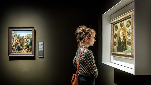 Een persoon kijkt naar een schilderij in een duistere ruimte.