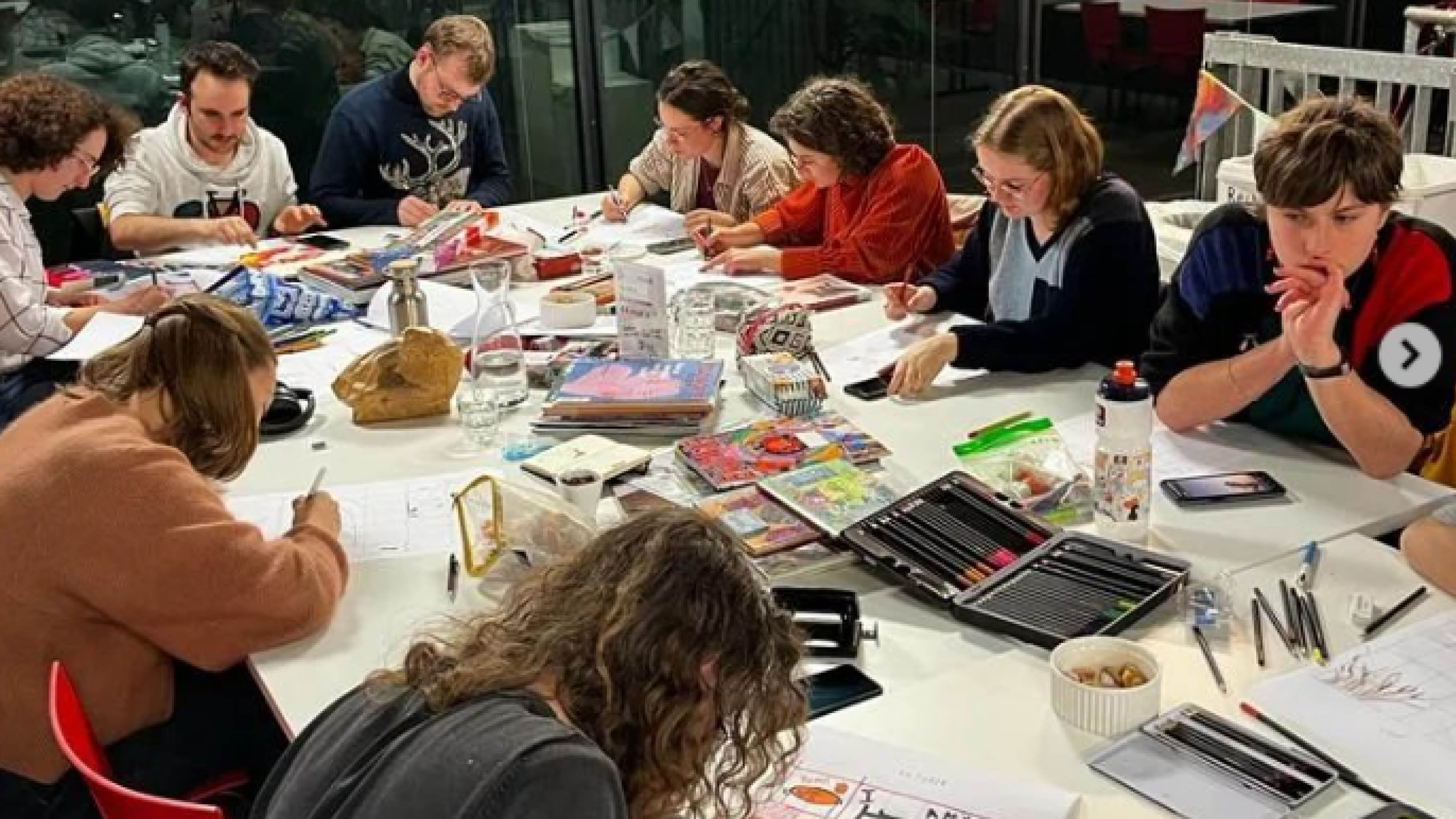 een groep jongeren zit aan een grote tafel en maakt zines