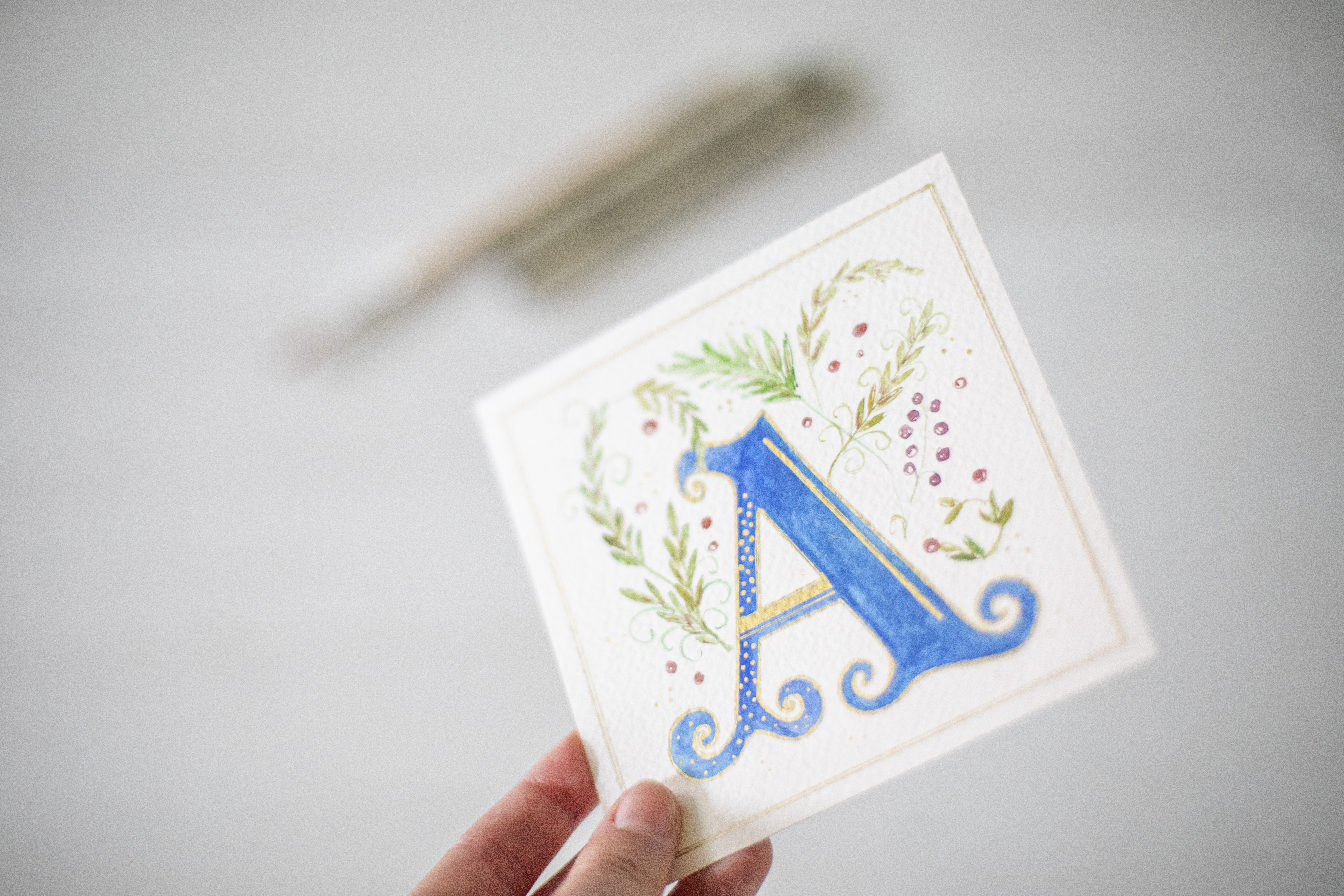 hand die een vierkantig papier vastheeft met een mooie letter A