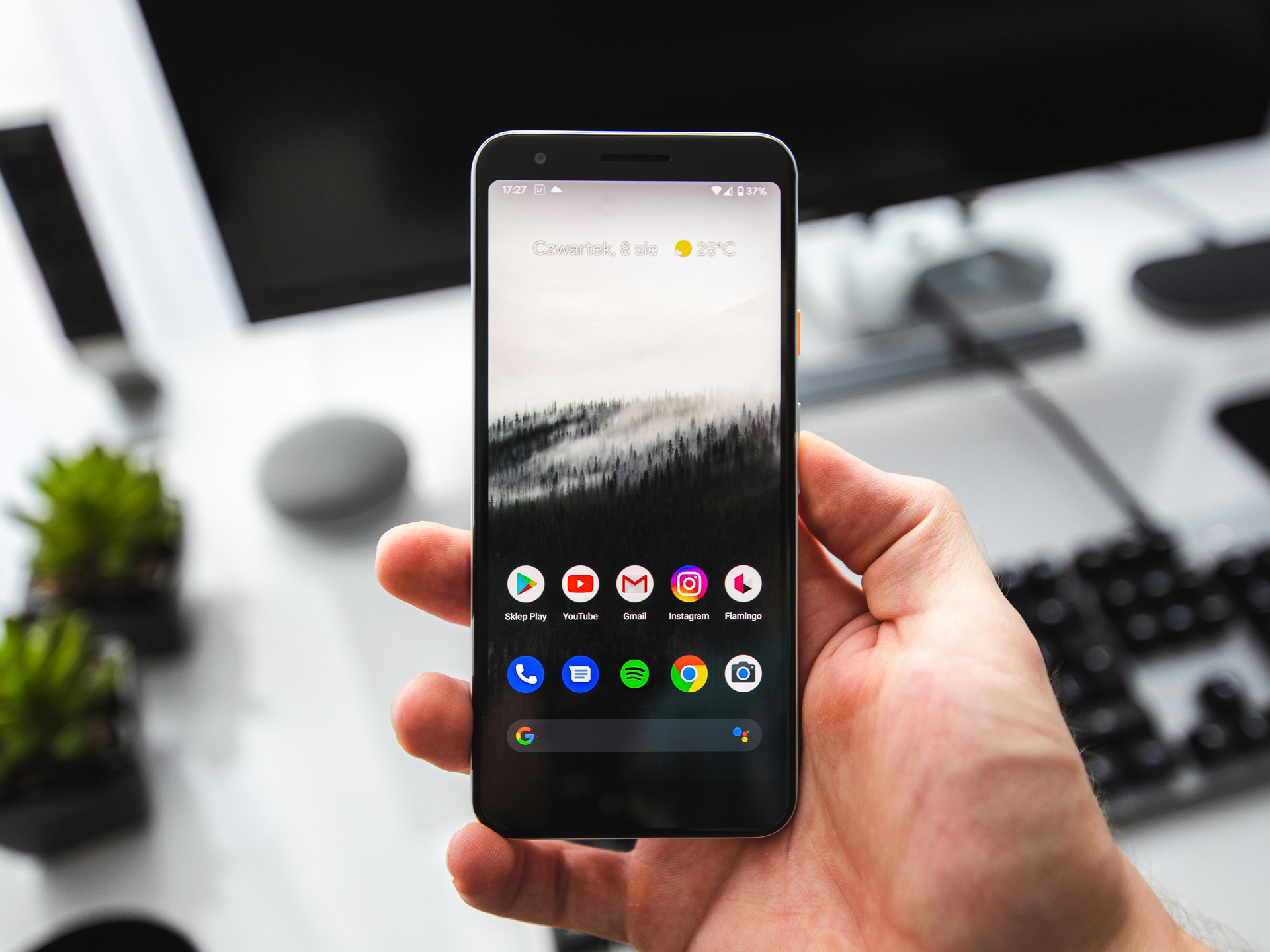 Hand die Android-smartphone vasthoudt waarop het beginscherm met een aantal apps is te zien