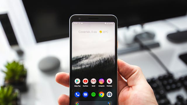 Hand die Android-smartphone vasthoudt waarop het beginscherm met een aantal apps is te zien