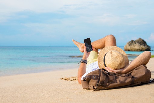 Persoon ligt op het strand en gebruikt gsm