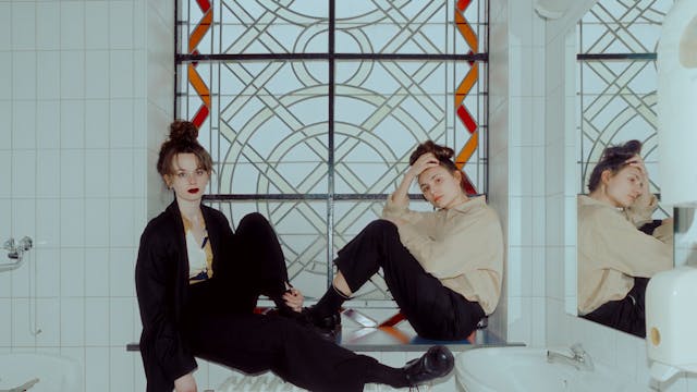 Kids With Buns poseren op een chauffage in een witte badkamer.